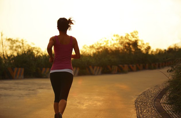 sporty woman morning exercise running on mountain driveway under sunrise