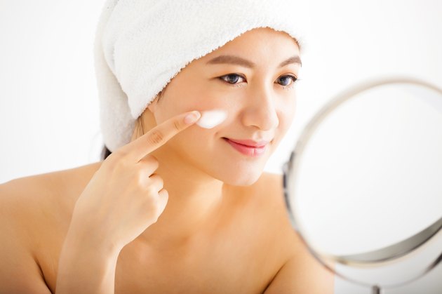 smiling woman applying cream lotion on face