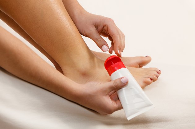 Woman putting ointment on bad ankle applying cream