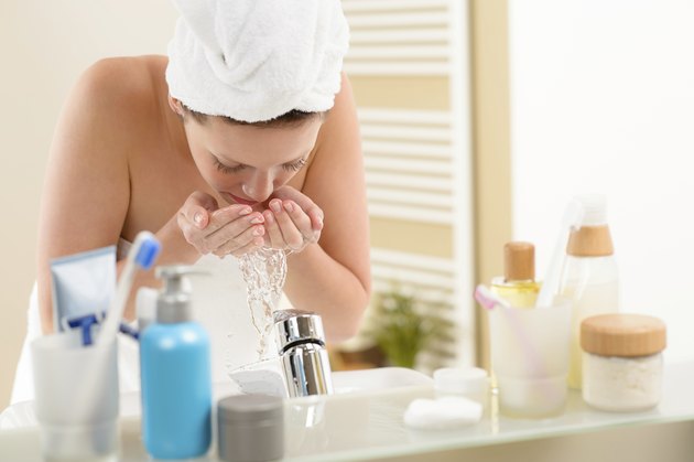 Woman washing face above bathroom sink