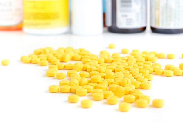 Heap of small yellow tablets (or pills) on white table