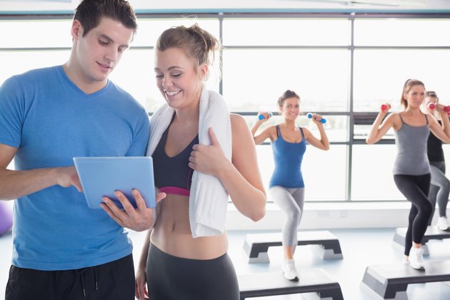 Trainer and woman talking while aerobics class lifiting weights