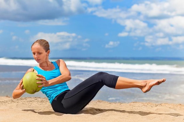 Fit woman exercising stomach muscle on ocean beach. Doing crunches.
