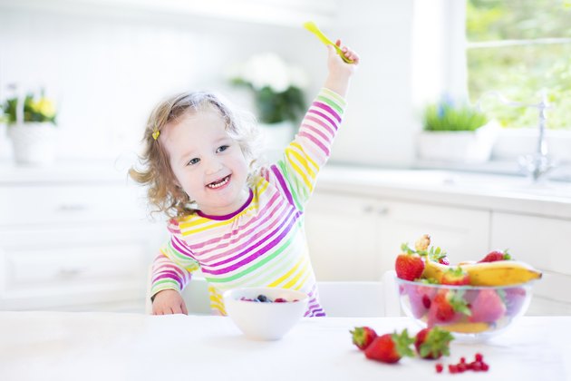 Toddler girl with curly hair wearing colorful shirt having breakfast
