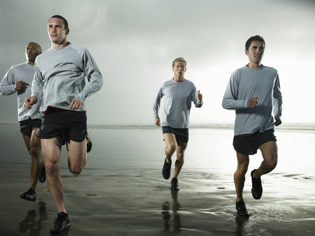 Four men running on beach by ocean