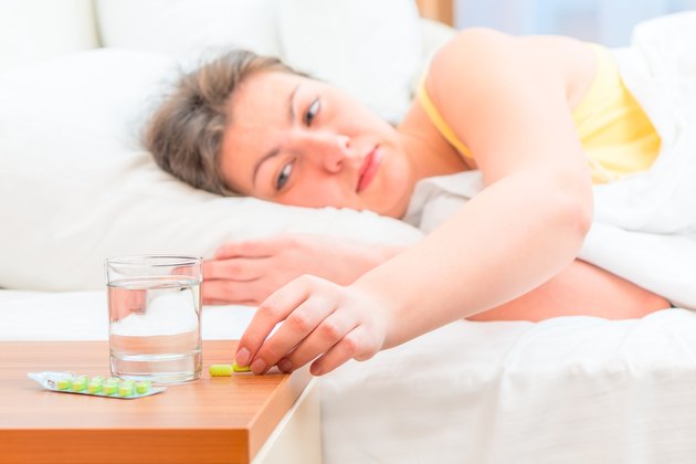 sick woman in bed reaching for pills