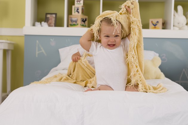 Child playing with blanket on bed