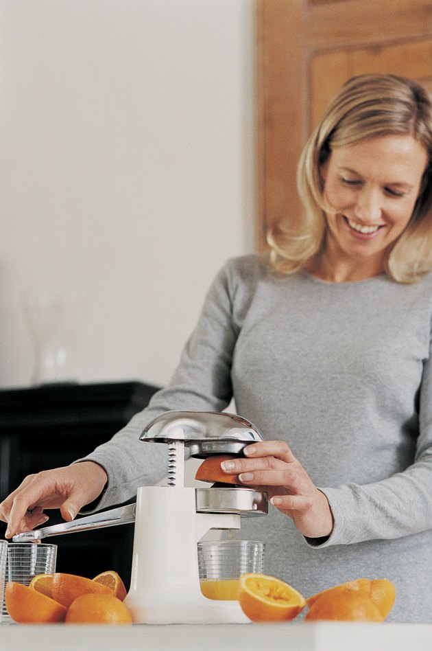 Smiling Woman Using a Juicer to Make Fresh Orange Juice in Her Kitchen
