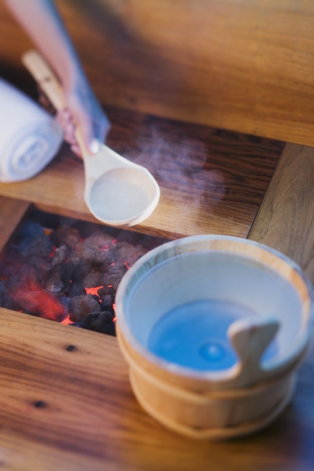 Person pouring water onto hot rocks in sauna