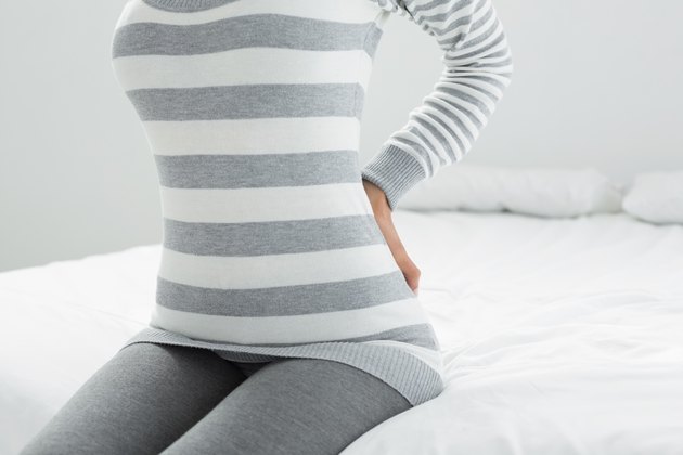 Mid section of a woman with back ache sitting in bed