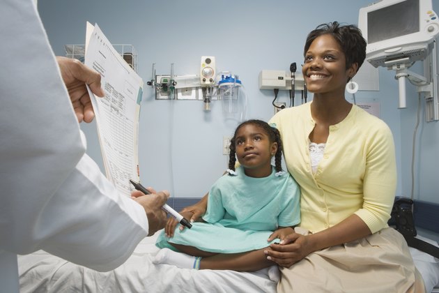 African girl in hospital bed with mother talking to doctor