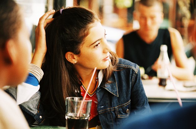 Teenage girl (14-16) sitting in a cafe with other people in the background