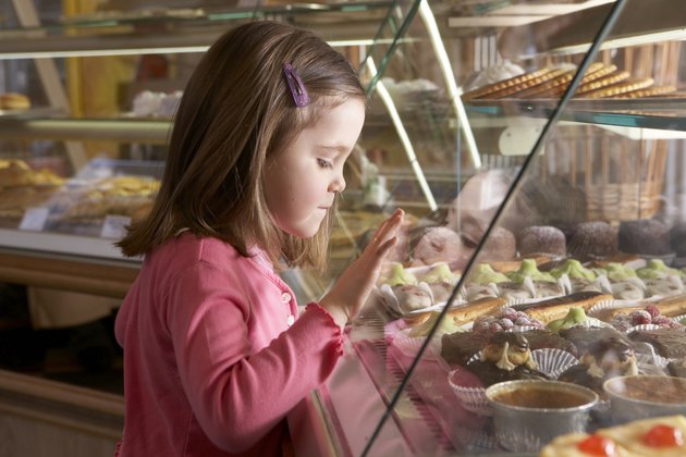 Young girl (9-11) looking at cakes in display cabinets, side view