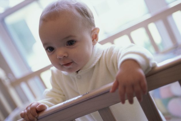 Close-up of a baby boy holding the railing of a crib