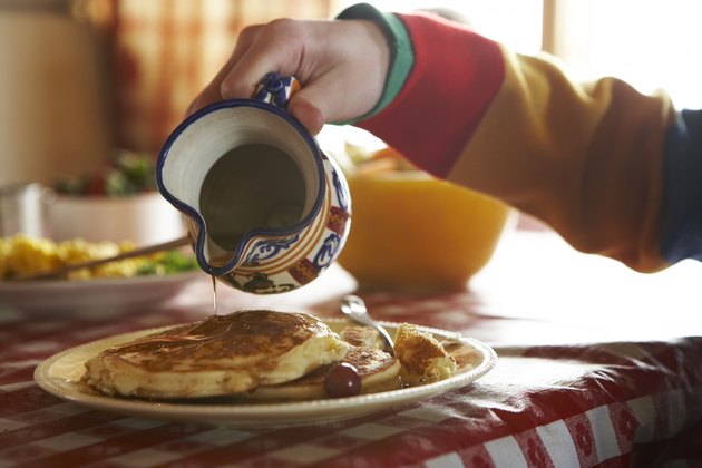Teenage boy (13-14) pouring syrup on pancakes