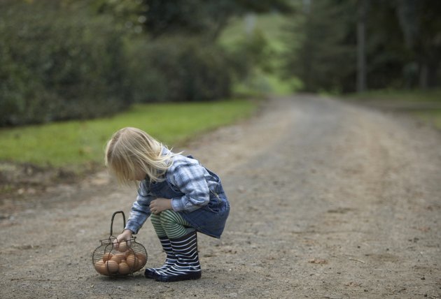 Young girl (3-4) squatting on road by basket with eggs, side view