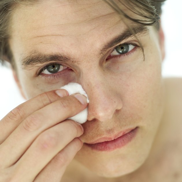 portrait of a young man cleaning his face with cotton wool
