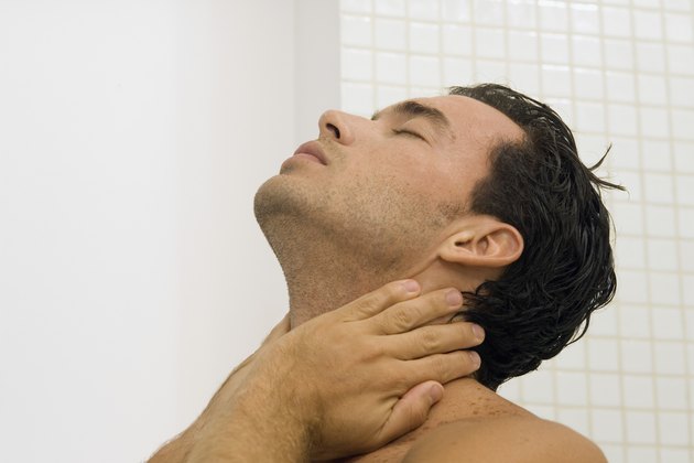 Young man standing in the shower holding his neck