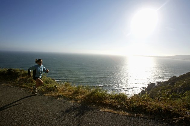 Woman jogging on road beside ocean, California, USA