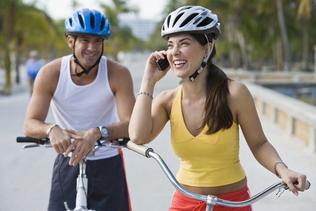 Hispanic woman on bicycle talking on cell phone while boyfriend waits