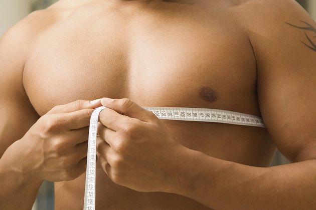 Young man measuring chest, close-up, part of