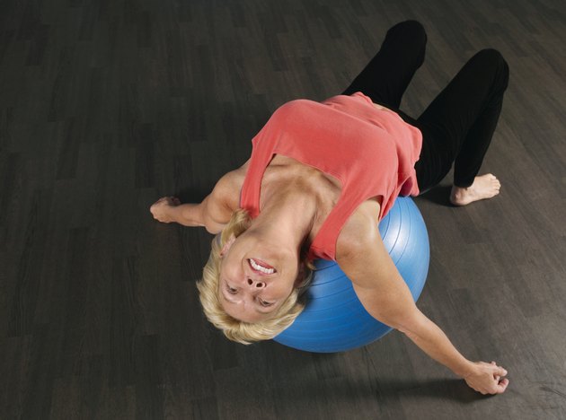 Mature woman using exercise ball, tilting head back, smiling
