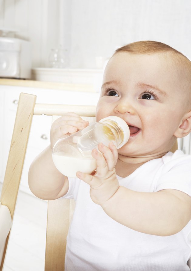 Baby girl (6-9 months) with bottle in high chair smiling, close-up