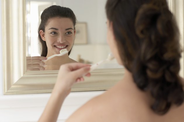 Young woman holding toothbrush, smiling, reflection in mirror