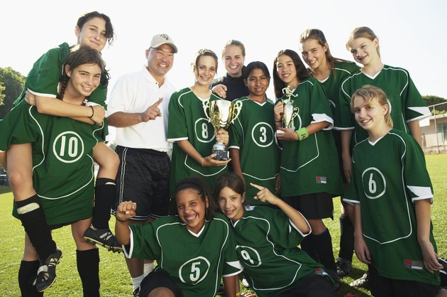 Football team (12-14) and coach with trophies, smiling, portrait