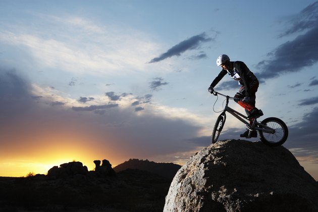 Bike rider balancing on rock boulder, side view