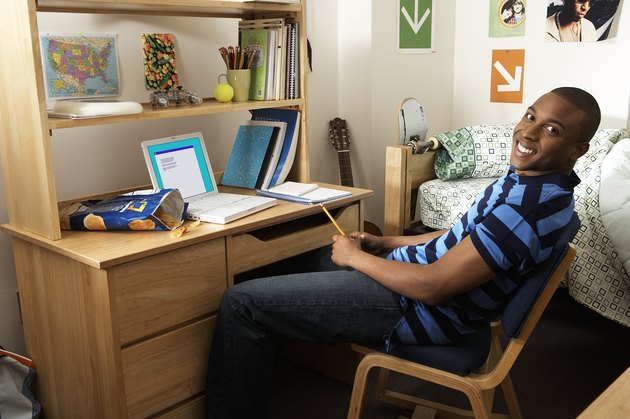 Young man sitting at desk in bedroom, smiling, portrait