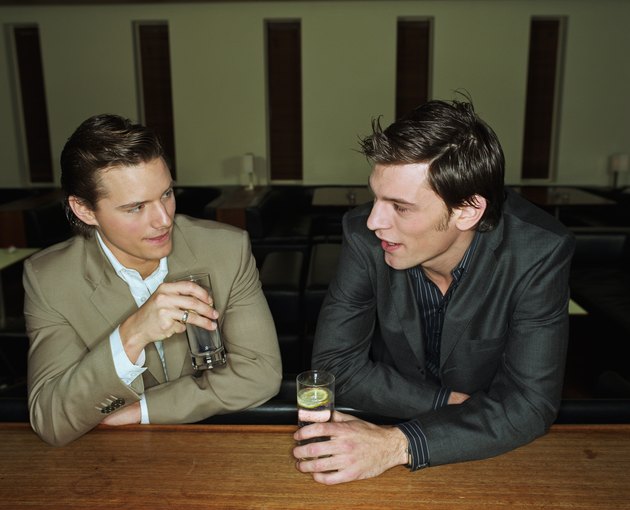 Two young men having drinks leaning on bar