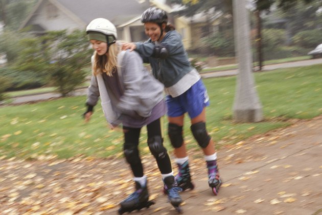 Two teenage girls (14-15) inline skating in park