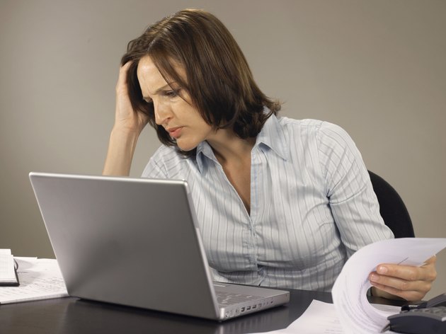 Woman using laptop resting head on hand, while turning page, frowning