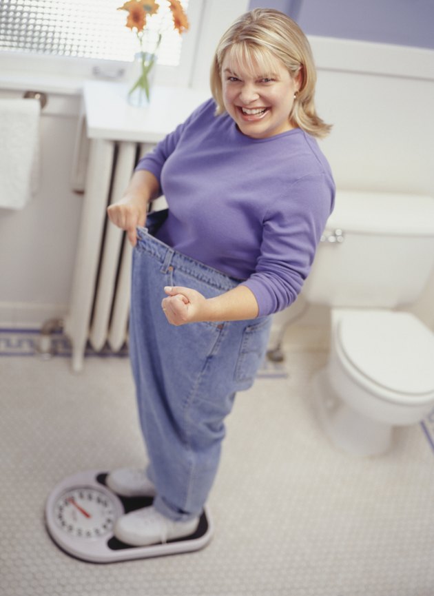 Woman on scale pulling jeans away from waistline to show weight loss, portrait