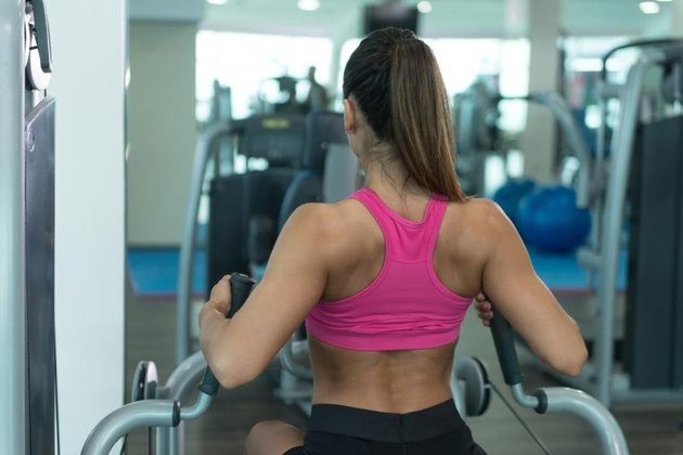 Young Fitness Woman Working Out Back On Machine In Fitness Center