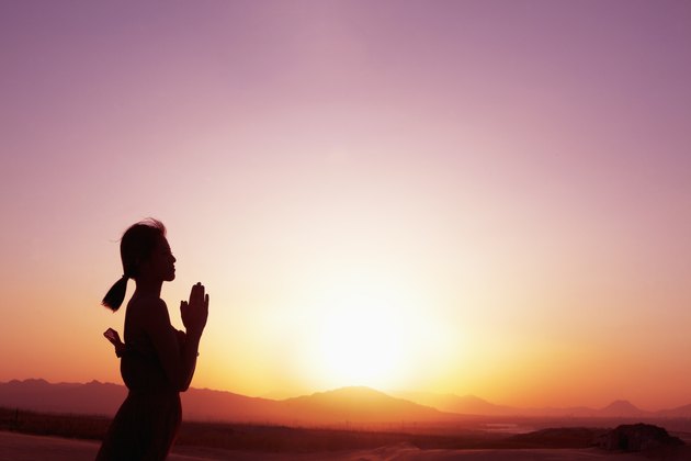 Serene young woman with hands together in prayer pose in the desert in China, silhouette, profile, sun setting