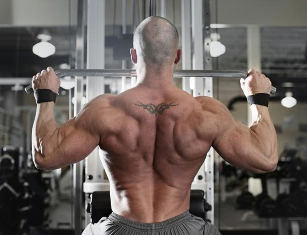 active and muscular man keeping his arms and back strong and fit by using gym equipment machinnes - filtered image