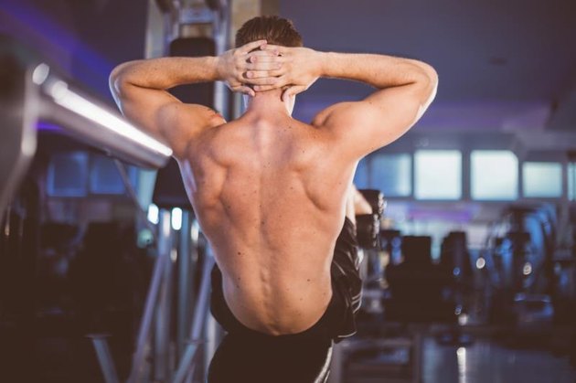 Attractive athletic back of young man doing incline bench sit-up exercise in indoor well equiped gym.
