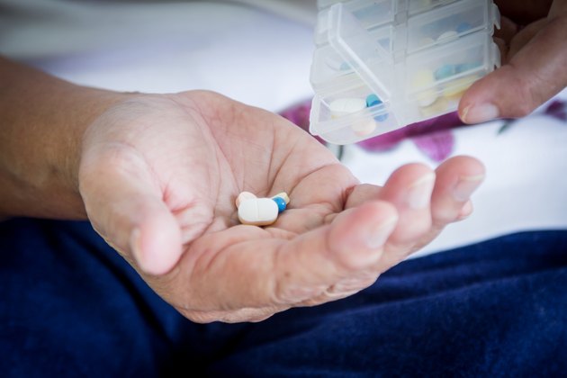 old woman hand pouring pills from a pill reminder box