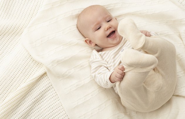 Baby girl (3-6 months) lying on blanket, smiling