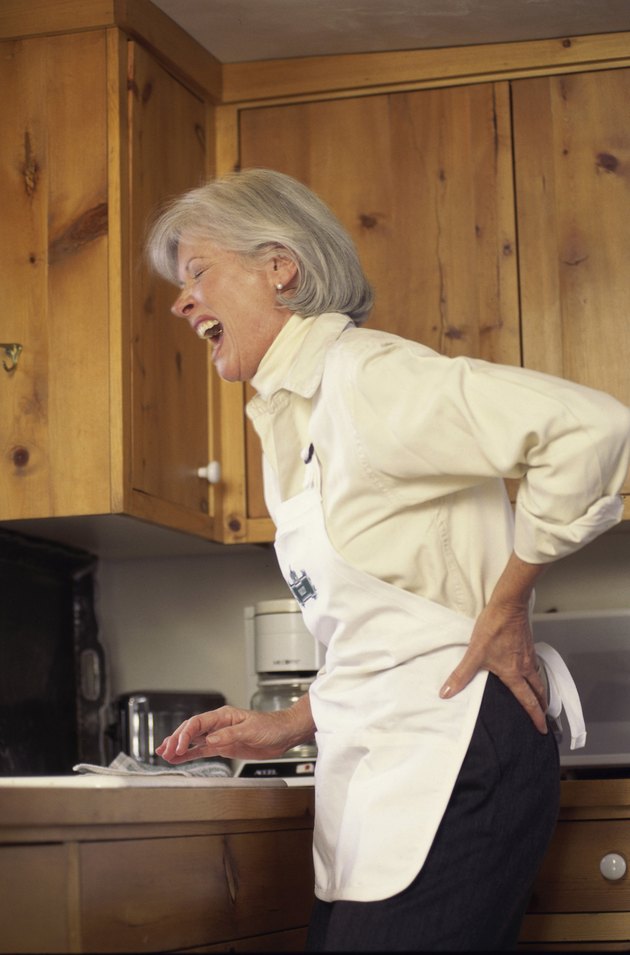 Woman standing in a kitchen holding her back in pain