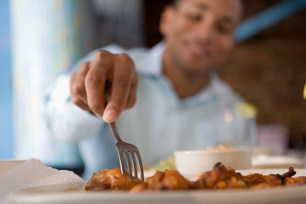 Man reaching for buffalo wing with fork