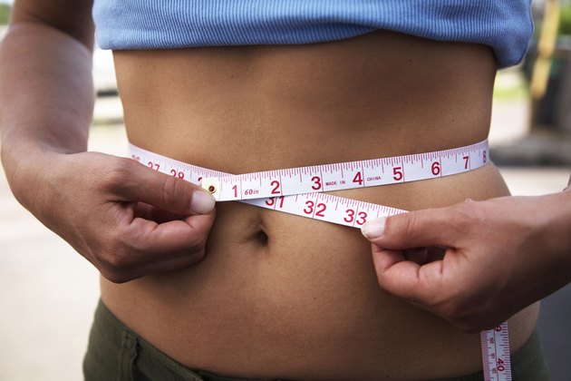 Mid section view of a woman measuring her waist with a tape measure