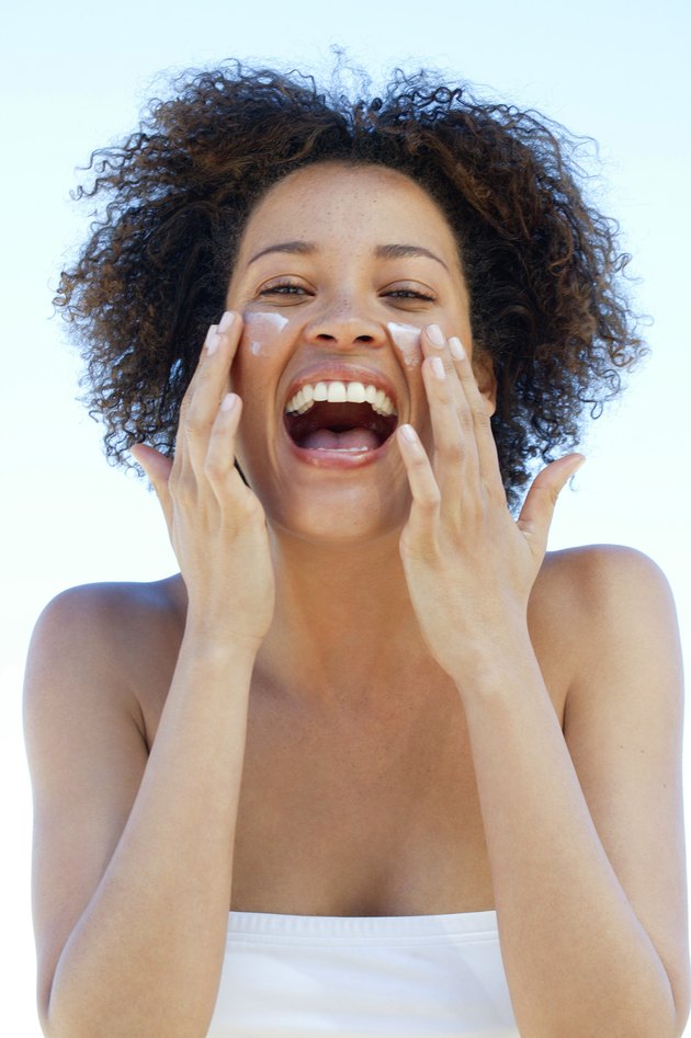 Woman rubbing suntan lotion on cheeks