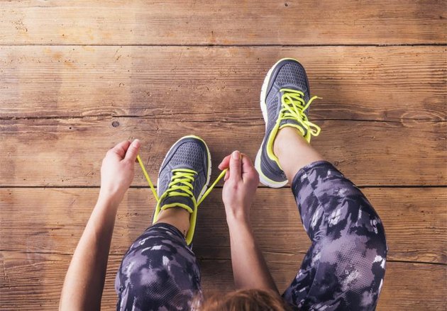 Unrecognizable young runner tying her shoelaces. Studio shot on wooden floor background.