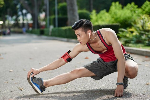 Asian young jogger stretching his legs outdoors