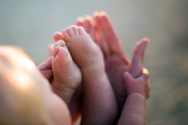 Little baby feet on mothers hands outdoors at backligh