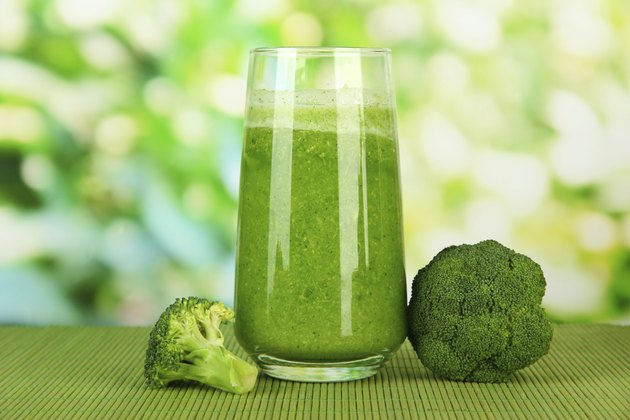 Glass of broccoli juice, on bamboo mat, green background