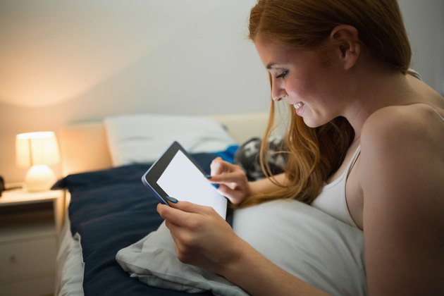 Attractive redhead using tablet lying on her bed
